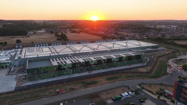 Google data centre Waltham Cross drone descent establishing shot at sunset, showing modern campus, roof structure, access roads and surrounding Hertfordshire landscape in golden hour light.