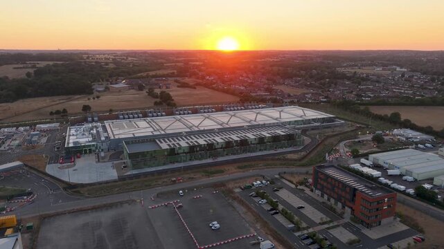 Google data centre Waltham Cross seen in a drone descent at sunset, revealing trading estate warehouses and roads as the A10 Great Cambridge Road enters frame near the end. Establishing shot.