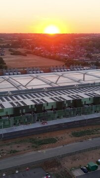 Google data centre Waltham Cross drone descent establishing shot at sunset, showing modern campus, roof structure, access roads and surrounding Hertfordshire landscape in golden hour light. Vertical.