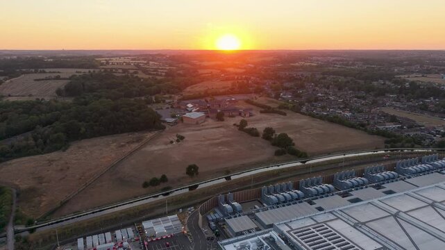 Google data centre Waltham Cross drone pullback at sunset, revealing service roads and surrounding fields and suburbs in Hertfordshire, England, with warm golden light on rooftops.