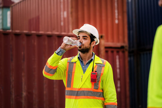 Container yard worker drinking bottled water during hot weather break at freight port. Hydration at Work, Heat Stress, Work Break, Industrial Safety, Outdoor Physical Labor
