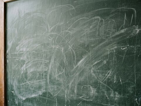 Old dark green school chalkboard covered with white chalk marks and smudges reflecting classroom environment for educational imagery and vintage rustic design themes.