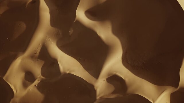 Aerial view of the Sahara Desert sand dunes featuring high contrast shadows and intricate golden sand textures across the vast landscape in Morocco.