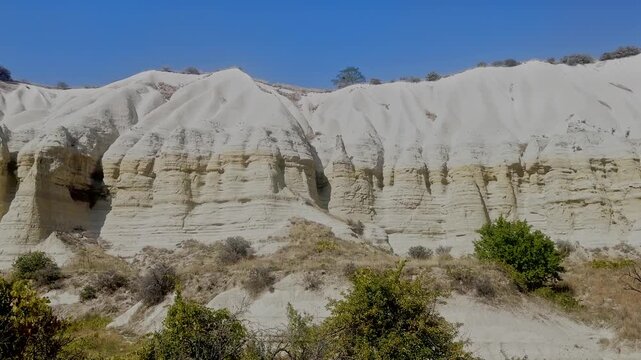White rock formations no visible action static scene, in desert landscape with clear blue sky, with white rock formations, green shrubs, from a static wide-angle shot perspective, nearby objects.