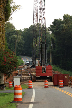 Heavy crawler crane and machinery operating at an infrastructure construction site surrounded by trees.