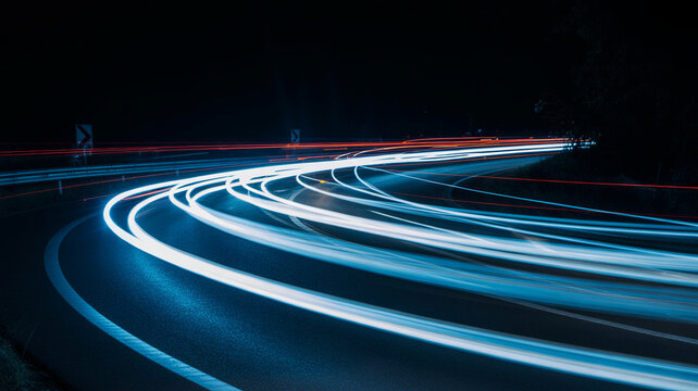 Long exposure light trails of car headlights moving along curved highway road at night stock photo
