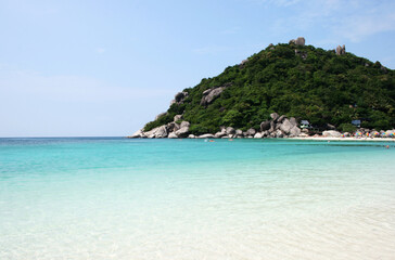 Fototapeta premium Crystal clear turquoise sea water near a tropical island with lush green hill and boulders
