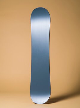 Teal snowboard standing upright with a high-gloss finish and yellow sidewalls against a golden background, blank mockup for rental graphics and retail