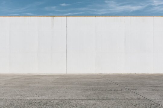 Bare cast-concrete wall rising above an open paved terrace, featuring a weathered, matte surface and atmospheric haze for architectural backdrops and copy space