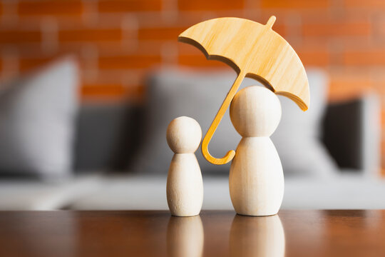 Wooden umbrella covering wooden family figures representing home insurance protection real estate property debt refinancing mortgage loan concept.