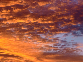 Fototapeta premium Dramatic orange sunset sky with glowing storm clouds fiery golden light purple twilight tones atmospheric cloudscape colorful nature background scenic evening weather
