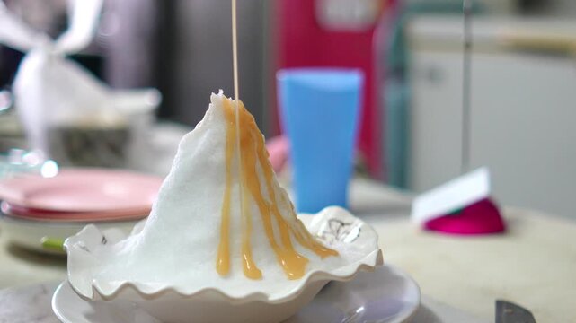 4K Close-up shot of condensed milk pouring over shaved ice mountain in bowl in dessert cafe, shaved ice bingsu sweet dessert refreshing food and cafe menu.