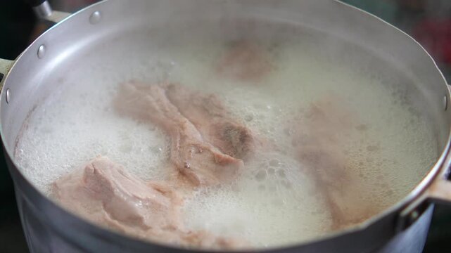 4K Close-up shot of pork ribs boiling in hot soup pot with steam and white bubbles cooking, Asian cuisine, soup stock preparation, recipe and food background.