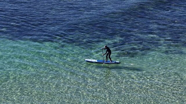 Aerial View of Person Paddleboarding in Clear Blue Ocean Water