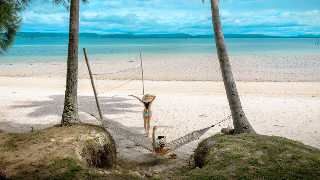 Top view of couple tourist are in motion of relaxing stay under coconut palm tree at the the edge of the sea beach,  trip summer on vacation of couple lover