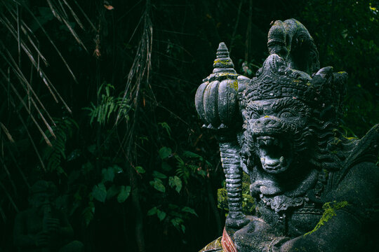 Balinese stone guardian statue stands with an open mouth and fierce expression. Its intricate monkey-like carving covered in moss