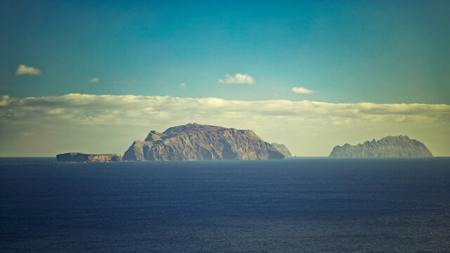 Furado, Portugal - 01.12.2025: Distant view of rocky Desertas Islands in deep blue Atlantic Ocean under a hazy sky with low white clouds