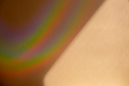 Macro shot of a rainbow light prism flare on a beige paper texture. Abstract colorful spectrum, creative shadow overlay, modern aesthetic background