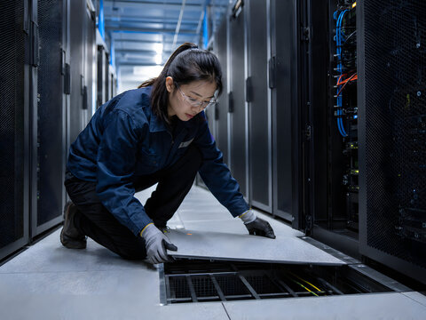 Qualified engineer inspecting underfloor cable management system in dark modern data center while performing routine maintenance on critical infrastructure hardware.