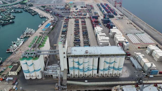Aerial view of the industrial Busan Port featuring large grain silos, rows of shipping containers, and docked vessels in the harbor in Busan, Busan, South Korea.