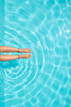 Overhead view of woman's feet relaxing in crystal clear turquoise swimming pool