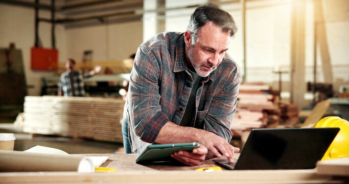Carpenter, research and man with tech in workshop, online and searching for furniture design on web. Warehouse, artisan and mature person with laptop, typing and planning for woodworking project