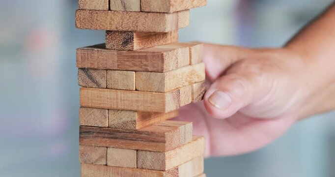 Hand removing a wooden block from a stacking tower game, strategy, decision making, risk, balance, problem solving, teamwork, and business concepts, close-up