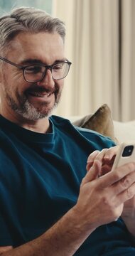 Smile, phone and man on sofa with connection, online communication and comic post on social media. Happy, digital and mature person in house with browse, funny text and meme reaction on chat app.