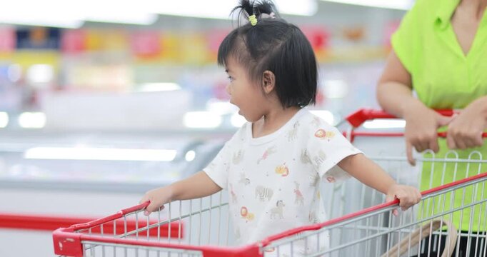 Young child sitting in a shopping cart while shopping in a supermarket, family shopping, everyday life, and consumer lifestyle, Asian Thai people