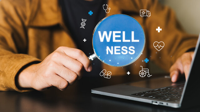Close-up of a person holding a magnifying glass with 'Wellness' text over a laptop screen