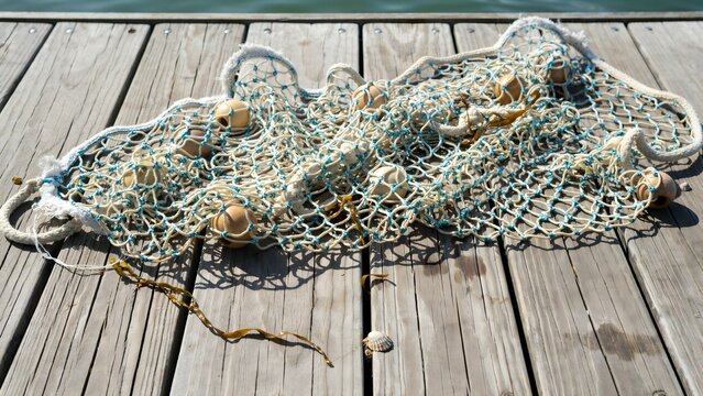 Fishing net with floats resting on a wooden dock by the water