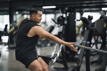 Fototapeta premium Man performing battle rope exercise or exercise with sled pull in gym