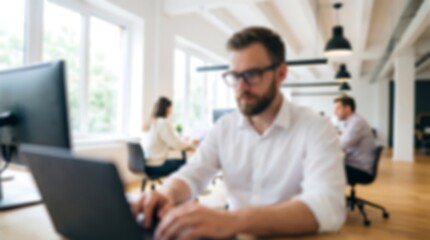 Fototapeta premium Focused bearded man wearing glasses and white shirt typing on laptop at workstation in blurred modern open plan office with colleagues working in background during busy business day