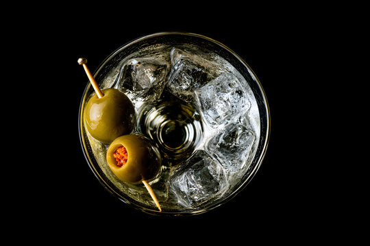 Martini, a glass featuring toasted olives on a toothpick, against a dark backdrop. An alcoholic chilled drink, taken head-on with space for a caption