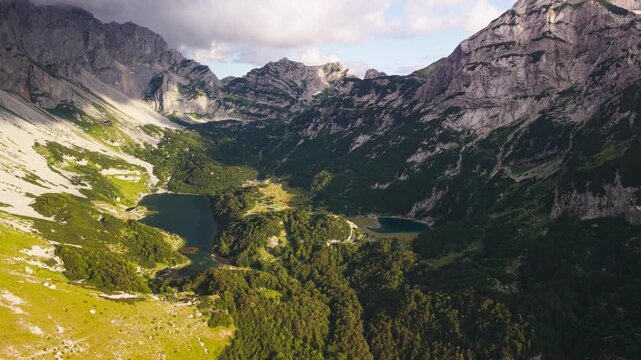 Drone reveal shot pulling back from hikers resting on grass to a wide aerial view of Skrcka Valley and Bobotov Kuk peak in Durmitor National Park, Montenegro