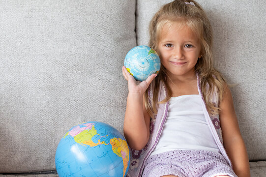 Happy child smiling while holding a mini globe, sitting on a sofa with a larger world globe, exploring geography and knowledge