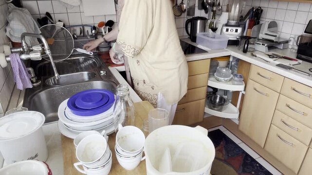 A static kitchen scene showing a woman organizing cutlery into a utensil holder while separating items that do not need washing before continuing the dishwasher loading process.