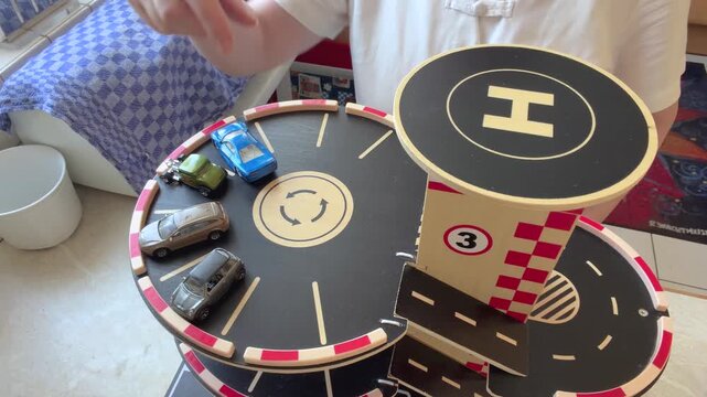 Close-up of an anonymous woman using her hands to park miniature toy cars in a wooden play garage. Static close-up from above