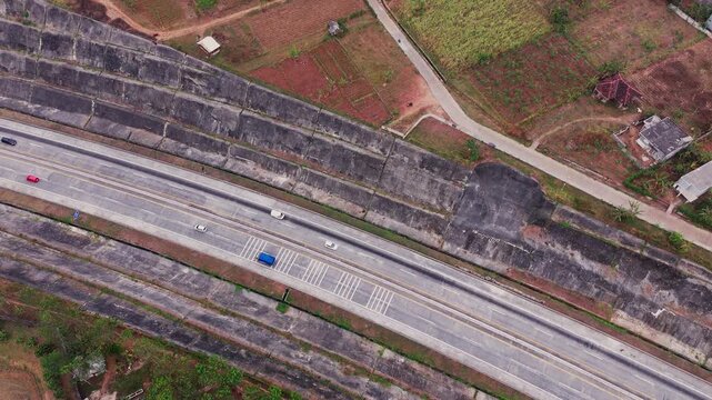 Aerial drone view of a modern multi lane highway and interchange in Indonesia, surrounded by buildings, trees, and urban infrastructure. Busy roads, vehicles, bridges, and overpasses create a dynamic 