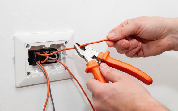 A technician holds pliers to connect electrical wiring inside a wall junction box. This focused shot is ideal for electrical repair and building maintenance concepts.