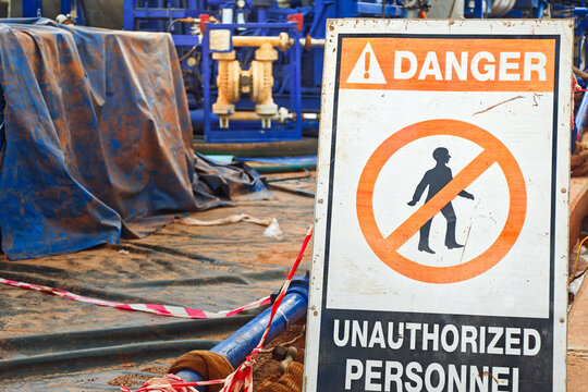 Danger, keep out sign with high-pressure pumping unit as background. Using to barricade hazard working area at industrial working site. Sign and symbol for industrial workplace, close-up.