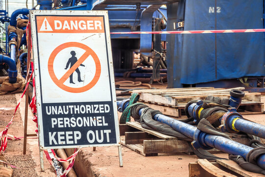 Danger, keep out sign with high-pressure pumping unit as background. Using to barricade hazard working area at industrial working site. Sign and symbol for industrial workplace, close-up.