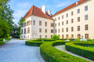 Obraz premium Visitors walk near Trebon Castle in Trebon, Czech Republic. The castle features historic architecture and well-kept gardens. People enjoy the outdoor space and the beauty of this site.