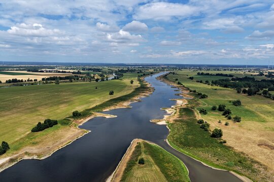 Aerial view of the Alte Elbe bei Bosewig river winding through lush green meadows and agricultural fields under a blue sky with scattered clouds in Wittenberg, Saxony-Anhalt, Germany.