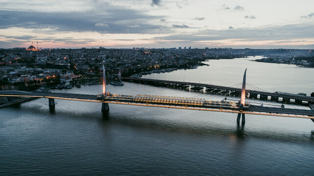 Aerial view of the Golden Horn Metro Bridge spanning the water at dusk with the illuminated city skyline and historic mosques in Beyoglu, Istanbul, Turkey.