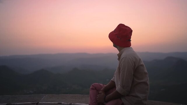 Man in bucket hat watching sunset over mountains in India