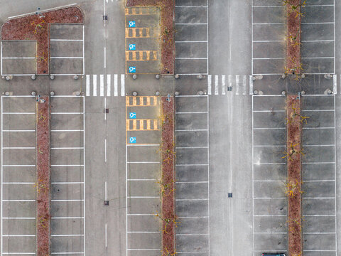 Aerial view of an empty parking lot with designated handicap parking spaces, pedestrian crossings, and rows of trees in planters in Leccio, Toscana, Italy.