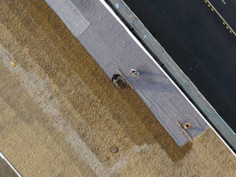 Aerial view of workers installing protective fabric and gravel on a flat rooftop next to a road in Belgrade, Serbia.