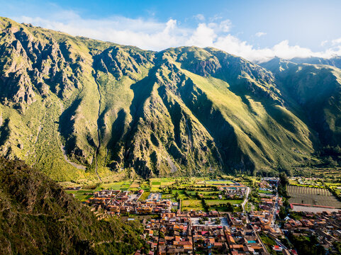 Aerial view of the historic town of Ollantaytambo nestled in the Andes mountains with stone buildings and surrounding agricultural fields in Ollantaytambo, Cusco, Peru.