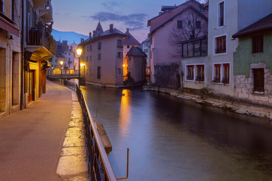 Cobblestone street with historic buildings and glowing street lamps in Annecy, France, during blue hour.
